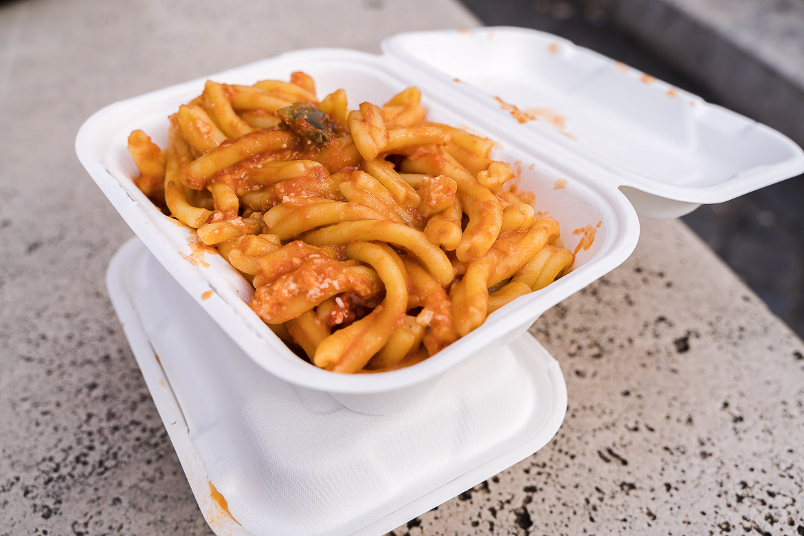 This is a close up of a container of fresh hot pasta with tomato sauce.