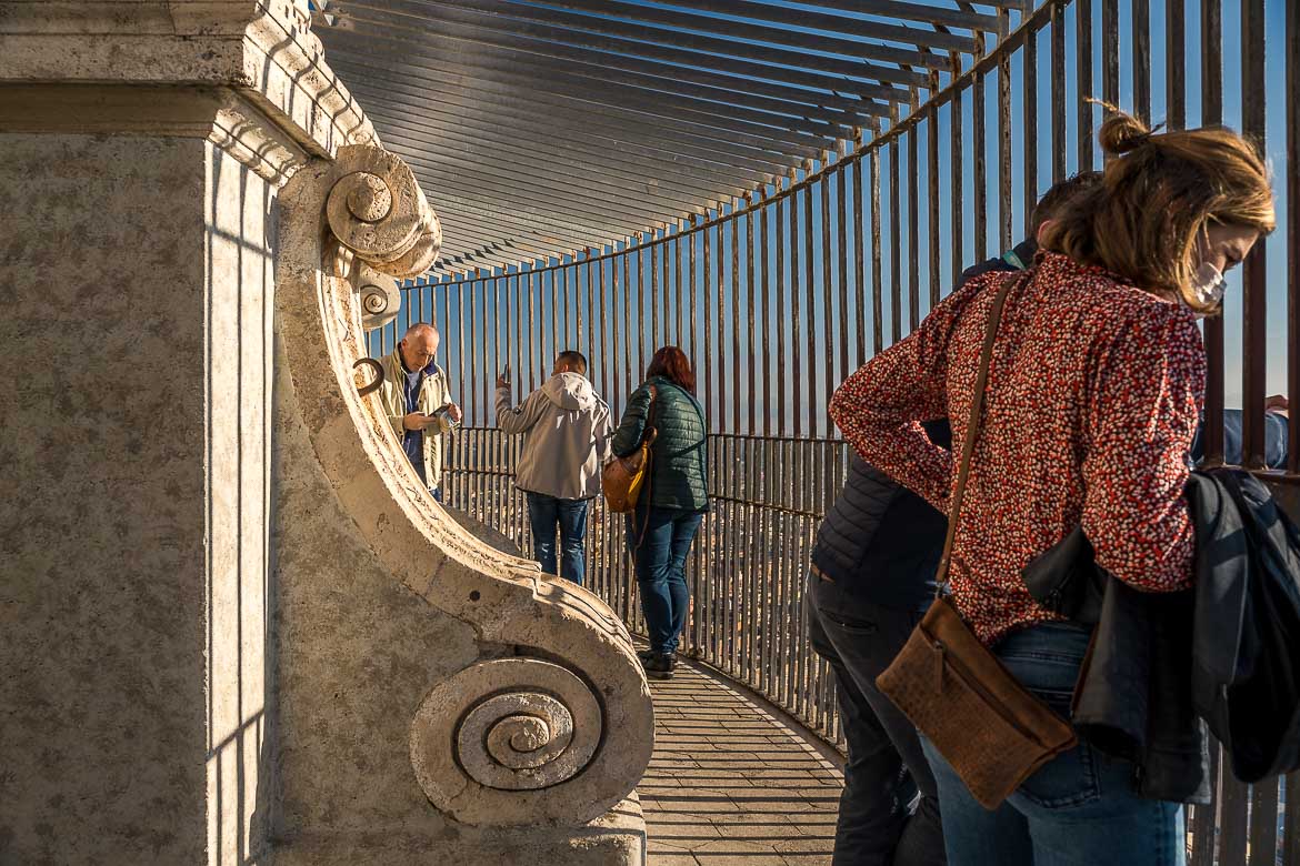 This image shows several people admiring the view through the rails from the top of the Dome of St. Peter's Basilica.