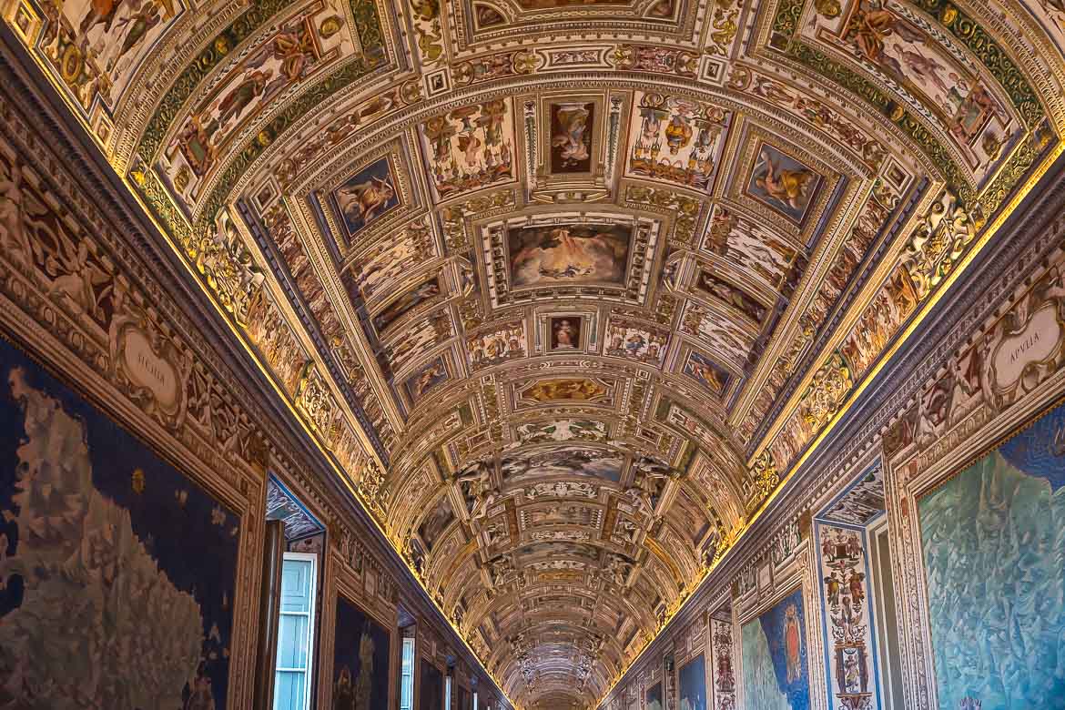 This image focuses on the elaborate ceiling with the gold details inside the Gallery of Maps. The walls are covered with maps.