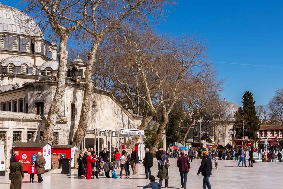 This photo shows the main square at Eyup. There are people walking or sitting and chatting. It's a bright spring day.