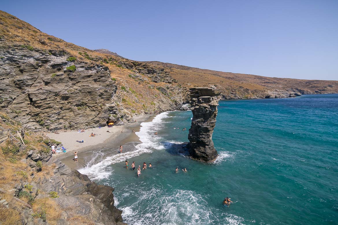 This is a panoramic shot of Tis Grias To Pidima Beach. It's a windy day so big waves are crashing on the silver hued shore. The 20m rock standing in the sea looks really impressive while people next to it seem super tiny.