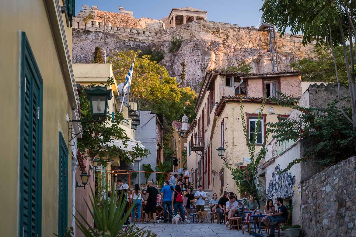 This image shows a quaint street in Plaka with beautiful cafés. In the background, there is the Acropolis.