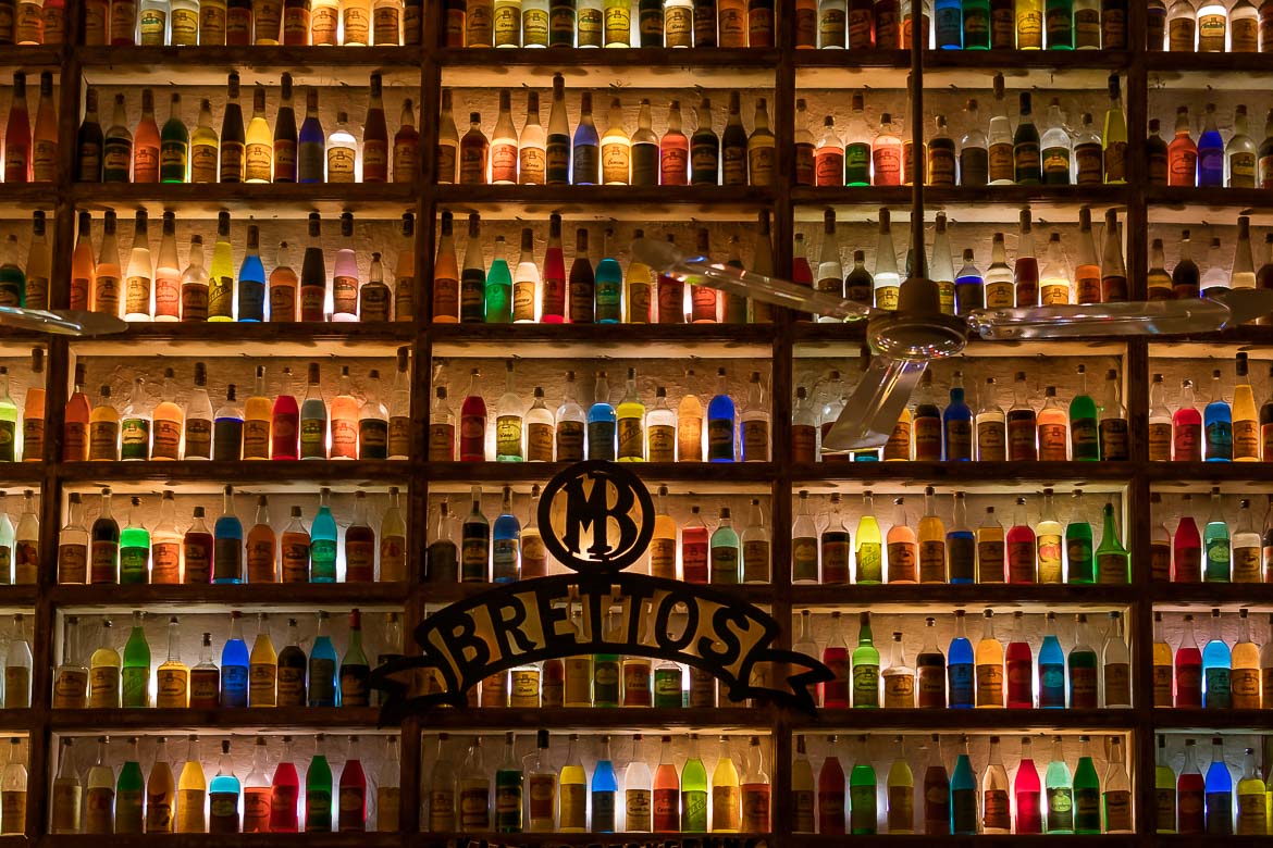 This image shows the interior of Brettos liquor store in Plaka. The entire wall is adorned with shelves filled with bottles of colourful liqueurs, which are among the best souvenirs from Greece to bring back home with you.