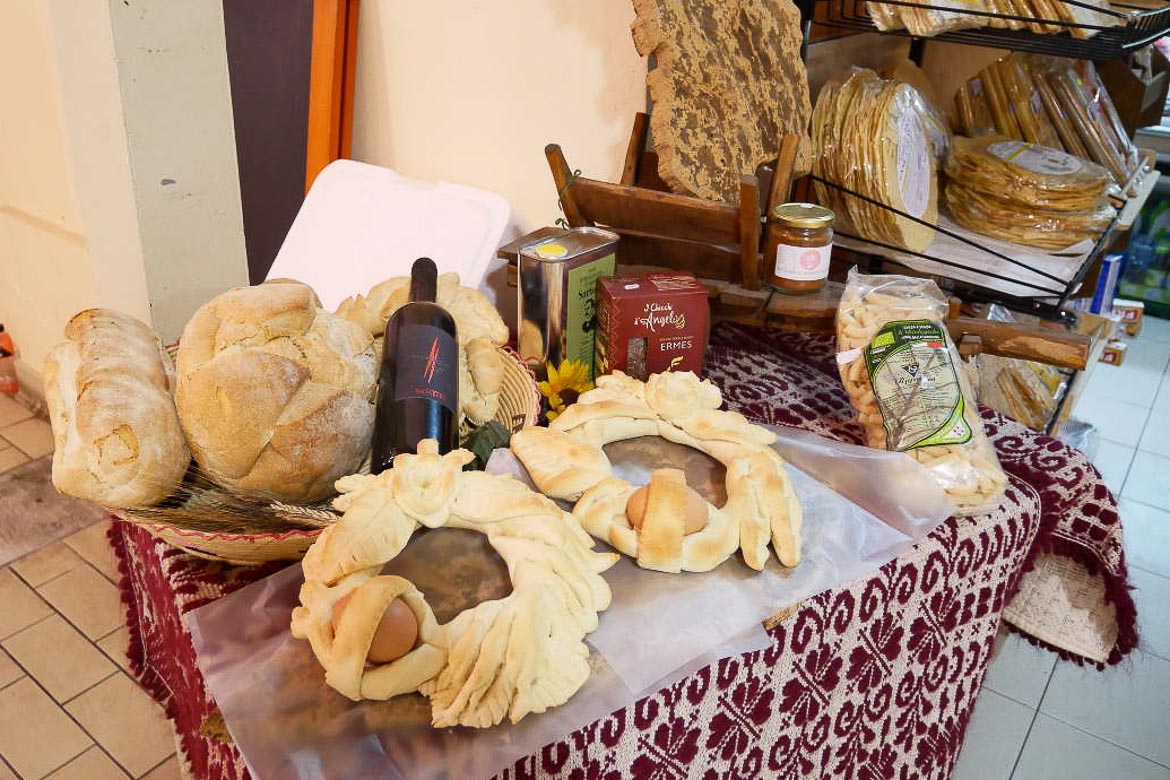 This picture shows a table on which there are two round loaves of Sardinia Easter bread. There are also some loaves of plain bread and a bottle of wine.