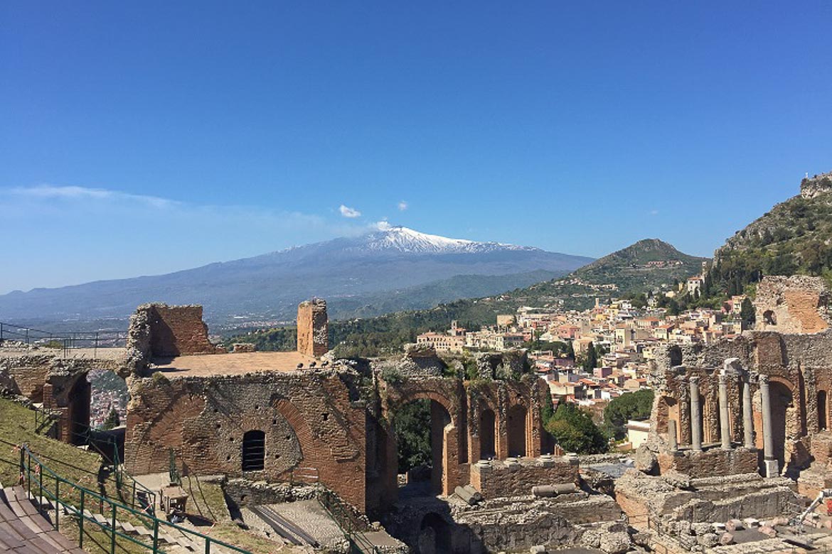This is an image of the Ruins of the Ancient Greek Theatre in Taormina. In the background, the snowy peak of Mount Etna is visible.