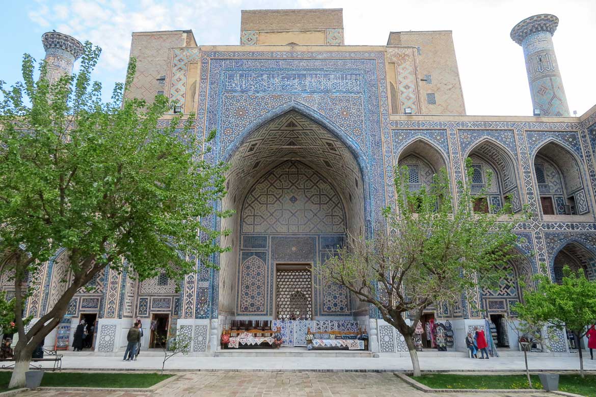 This photo shows a historical building in Samarkand, Uzbekistan. The country boasts unique, breathtakingly beautiful architecture. The madrassa pictured here has a facade covered in light blue and golden tiles.
