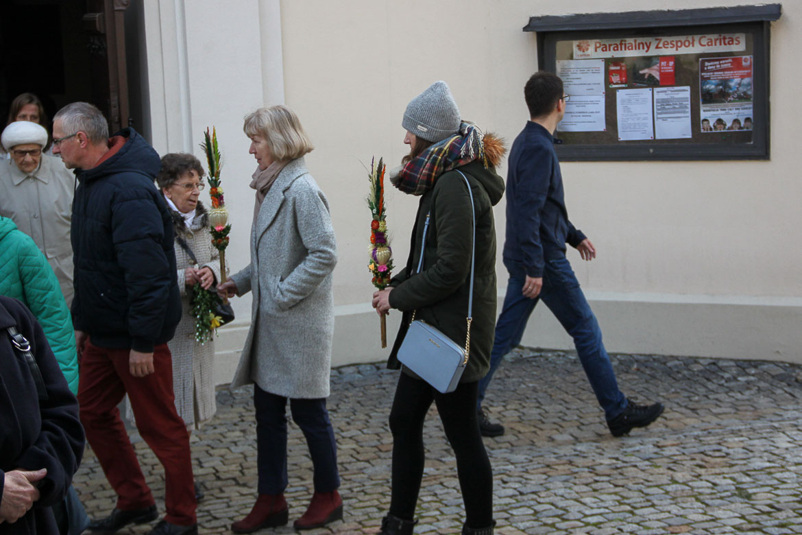 This image shows people outside a church on Palm Sunday holding Polish Easter Palms. The latter are bouquet-like colourful creations.
