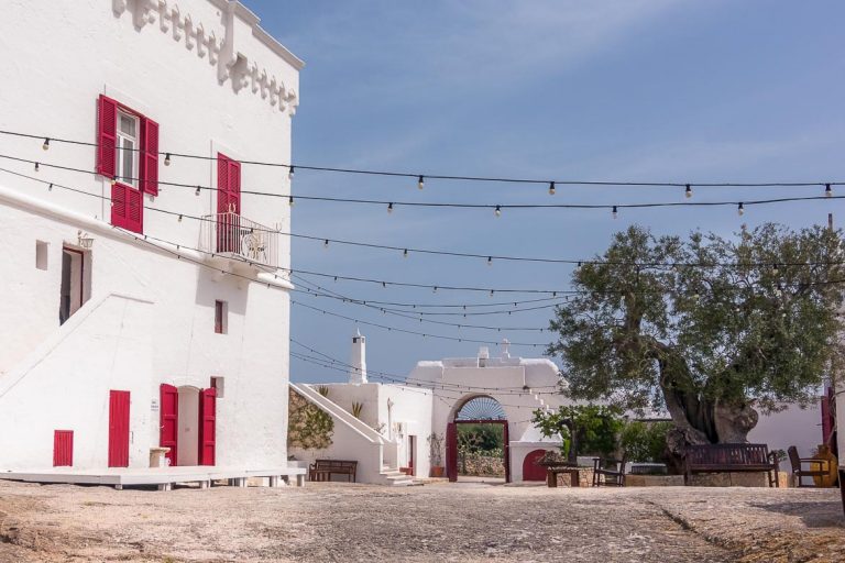 This photo shows the gorgeous central courtyard at Masseria Torre Coccaro. There is a whitewashed building on the left with bright red windows and doors. Masserie are typical to Puglia region. This is why we chose this photo to be the featured image of our article Best Places to stay in Puglia: An essential guide.