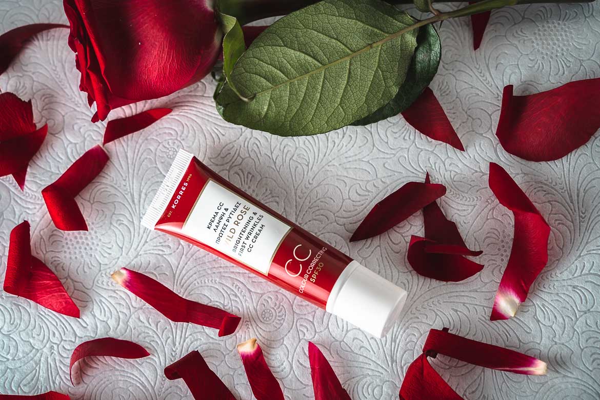 A Korres face cream in a red-and-white tube next to a red rose and surrounded by rose petals. Beauty products are among the best souvenirs from Greece.