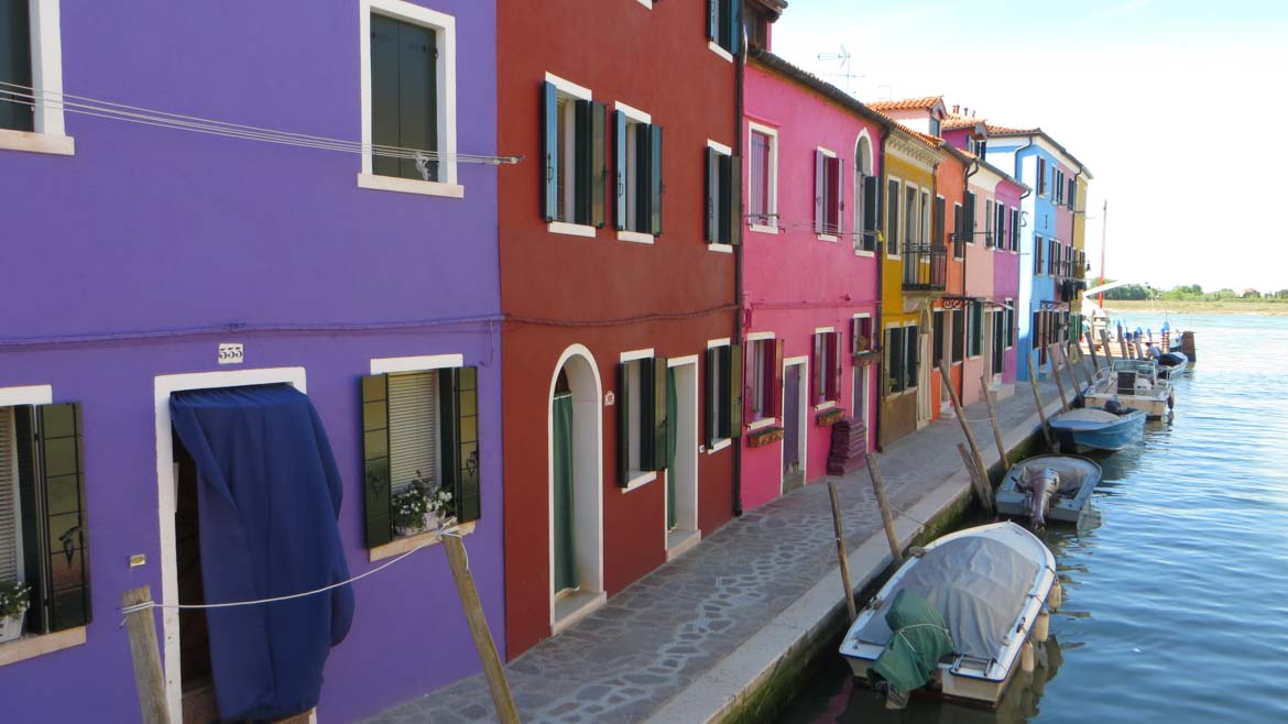 This photo shows a row of vividly coloured houses on the island of Burano near Venice, Italy. Venice islands, the perfect Venice day trip.