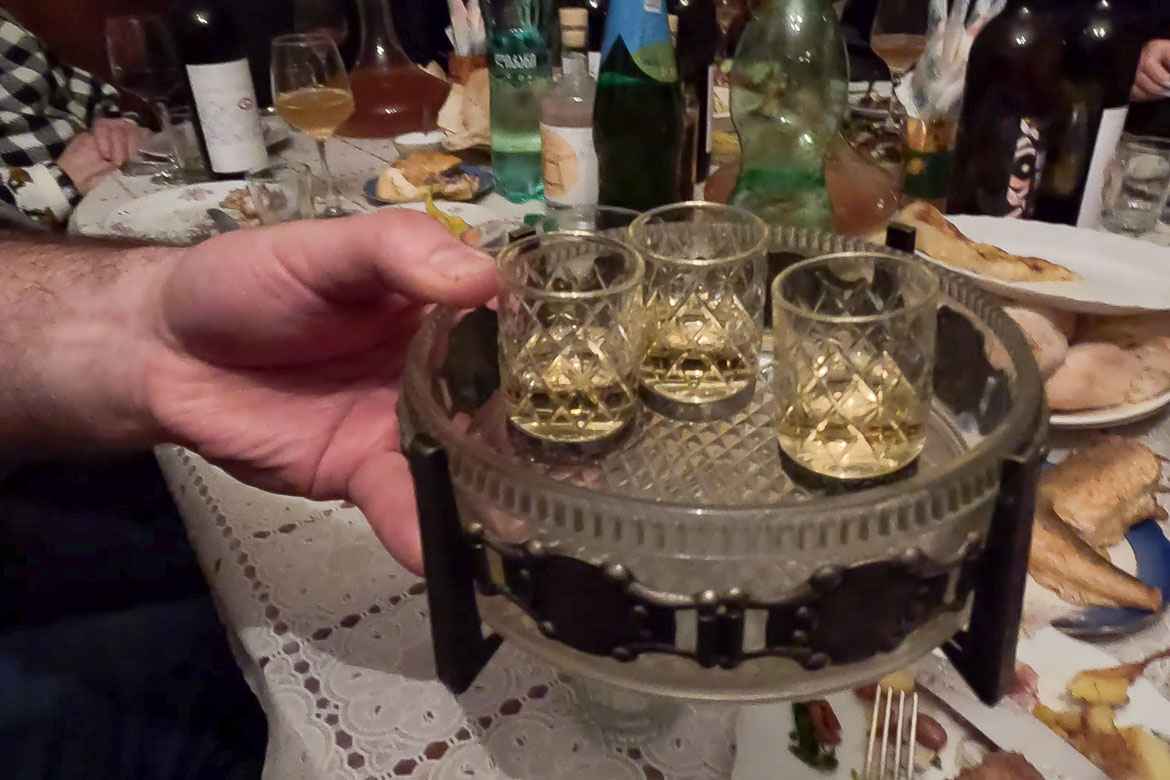 A hand offering a tray with chacha shots.