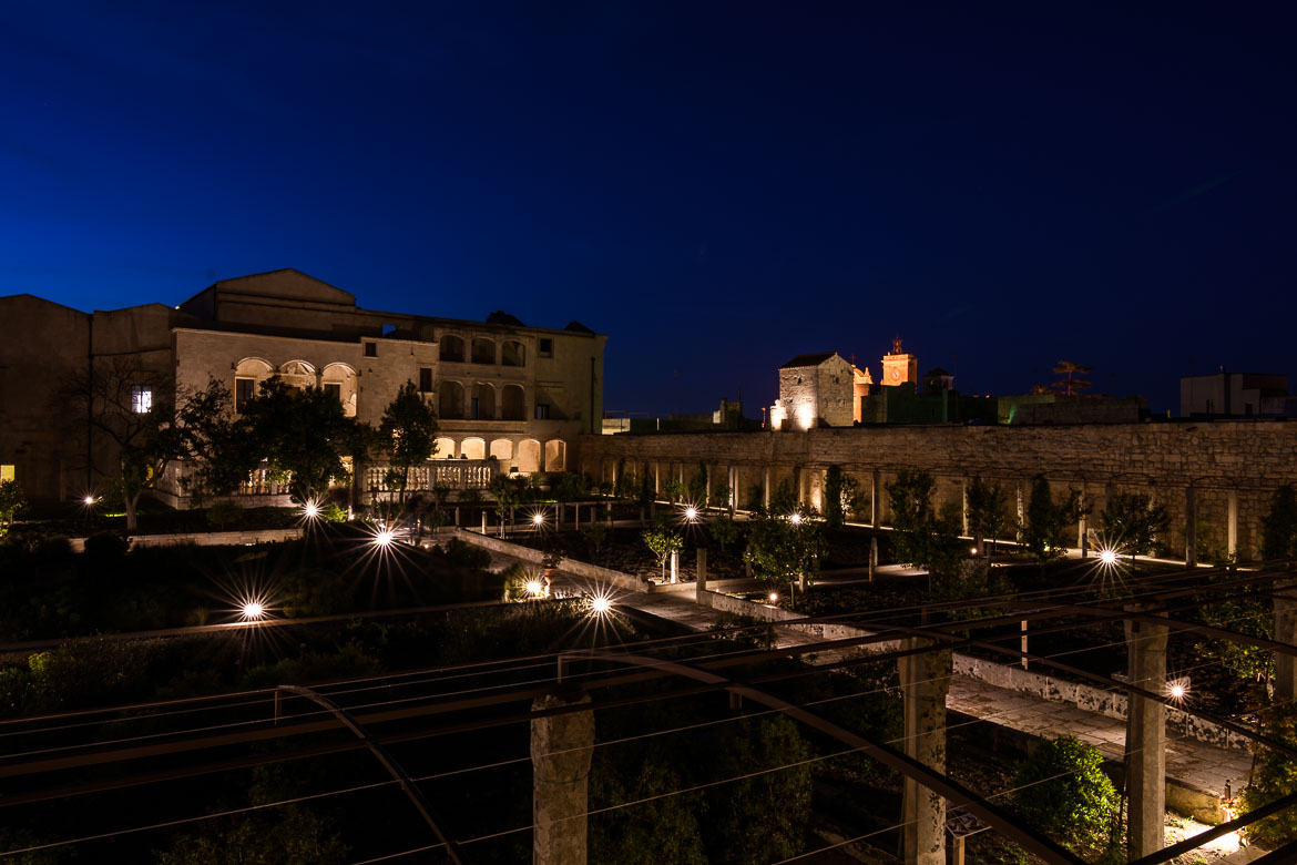 This photo was taken inside the garden of Palazzo Marchesale in the evening. The garden and the castle are dimly lit. 