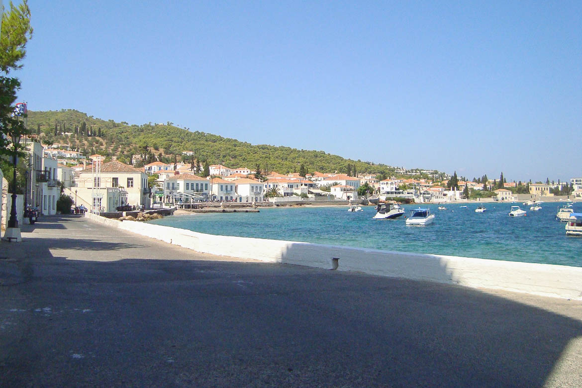 The car-free promenade in Spetses, one of the best Greek islands without a car. The promenade is lined with neoclassical buildings and small boats are moored in the harbour.
