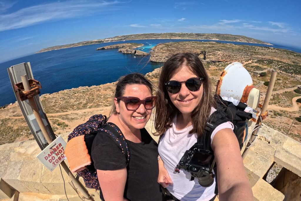 This image shows a selfie photo of Maria and Katerina from the Saint Mary's tower terrace. A panoramic view of the Blue Lagoon is in the background.