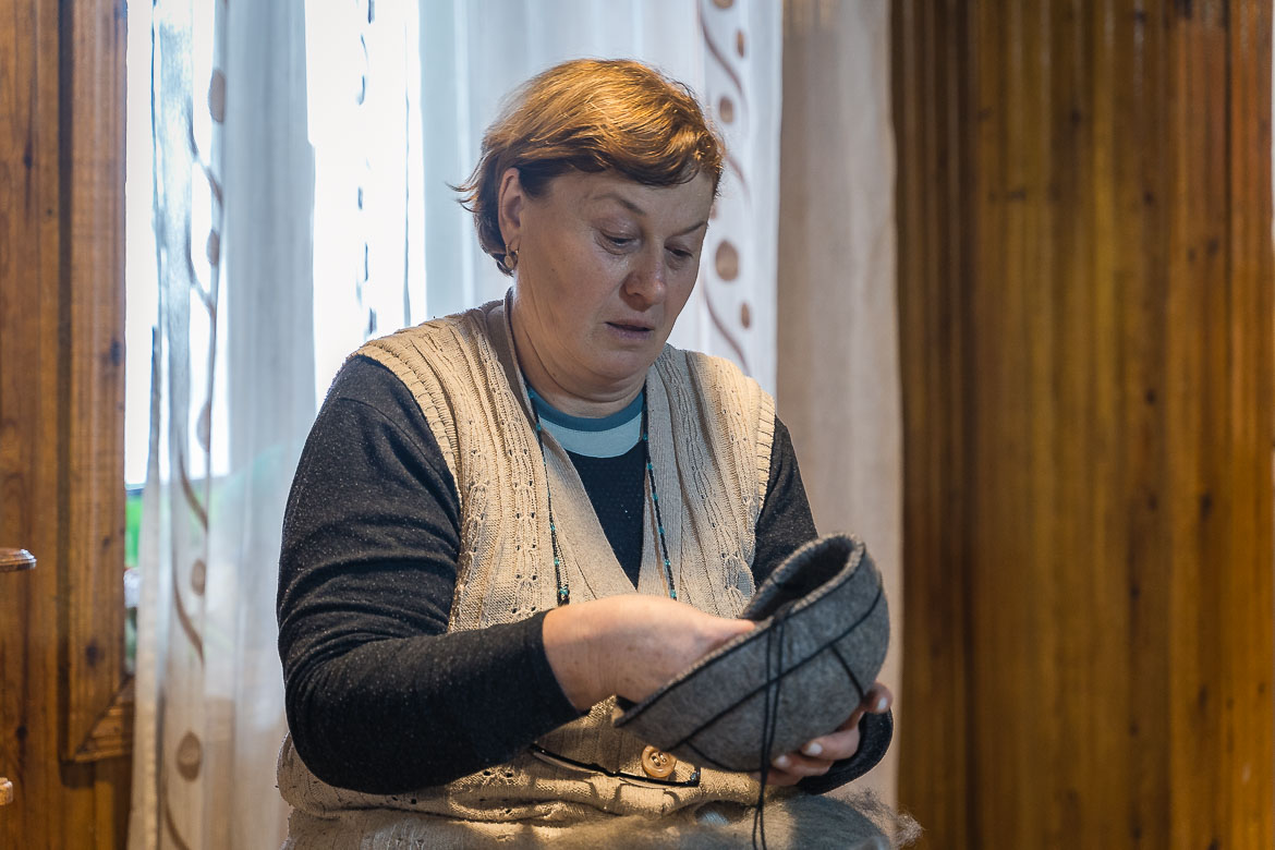 A woman is making a traditional Svan hat. The hat is made of wool and it's grey with black strings.
