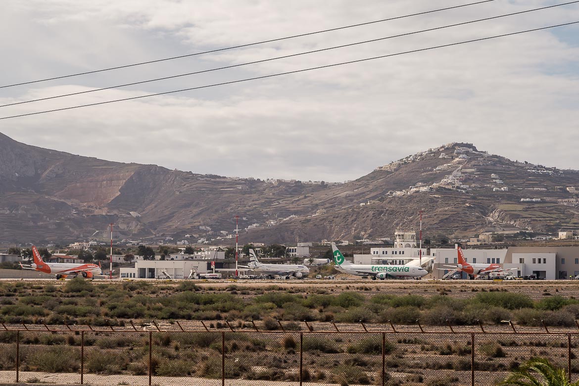 This image shows Santorini airport from a distance. There are two Easyjet airplanes, one Transavia and one Aegean.