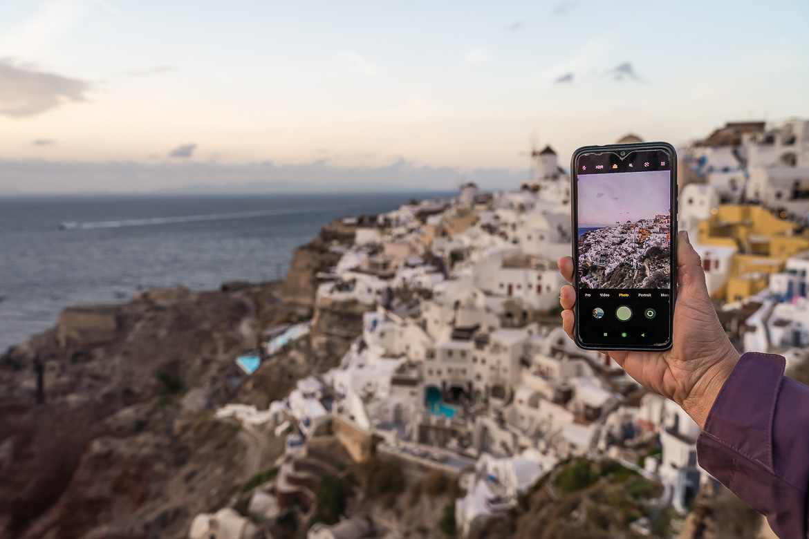 This image shows Maria holding a cellphone to take a photo of Oia in Santorini.