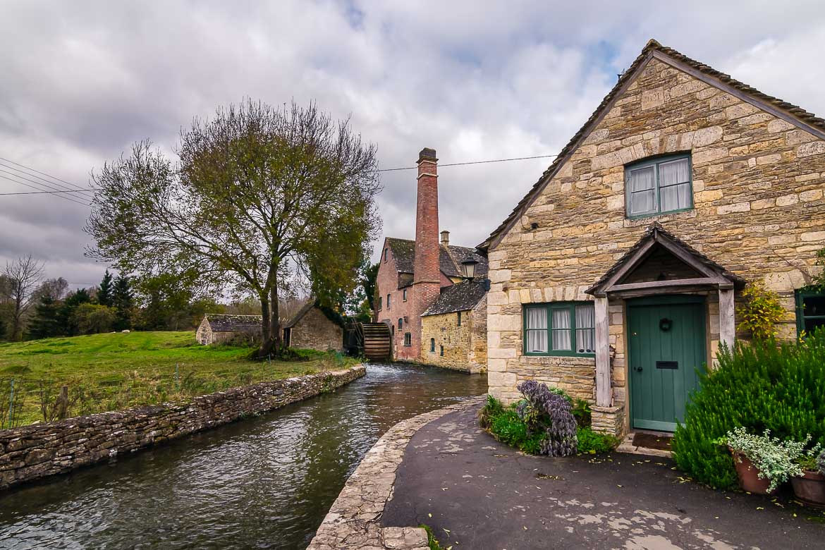 This image shows an old mill and a stone house by a stream in the Cotswolds, England.