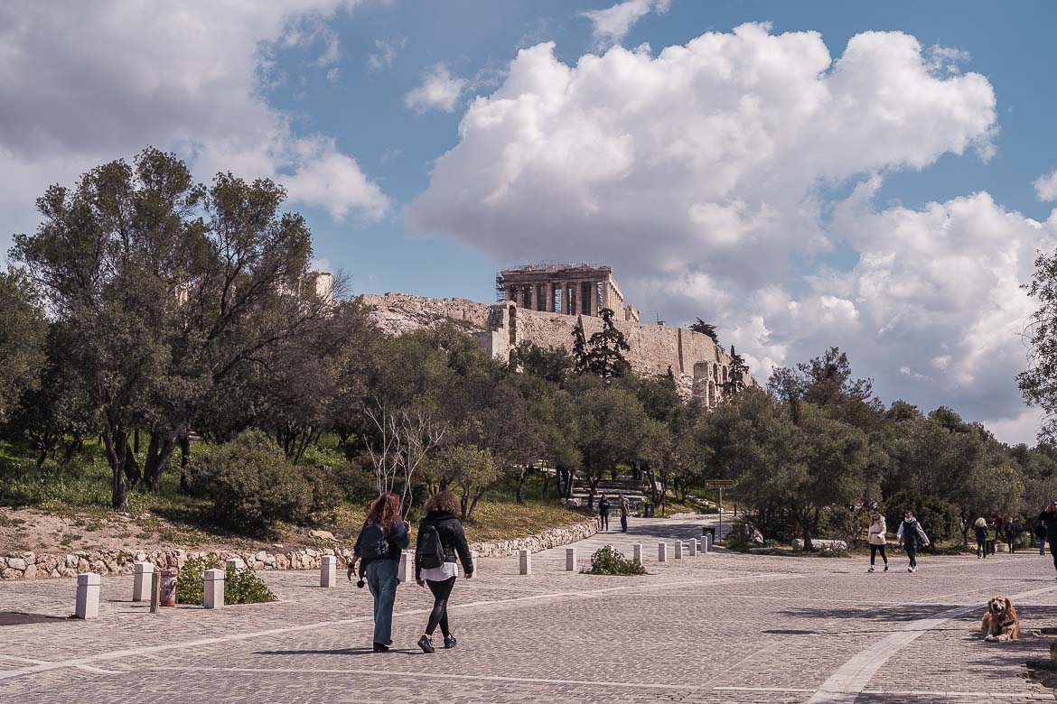 This image shows the Acropolis of Athens under a gloriously cloudy sky as seen from the gorgeous pedestrianised Dionysiou Areopagitou Street.