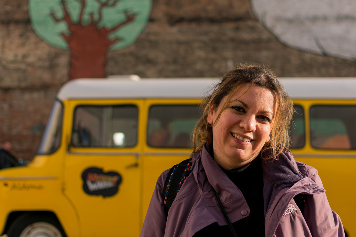 Maria smiling for the camera. In the background, a yellow Nysa van.