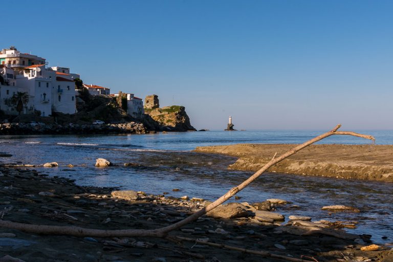 View to Chora and Tourlitis Lighthouse from Paraporti Beach. We've chosen this to be the featured image of our article 15 unique things to do in Andros Greece and full Andros Guide.