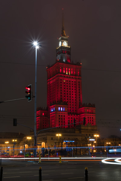 The Palace of Culture and Science at night, illuminated by red lights.