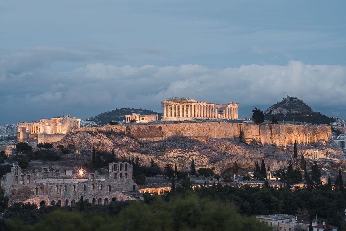 This image shows a panoramic view of the Acropolis at dusk. When planning a trip to Greece, make sure you catch the sunset at the Acropolis.