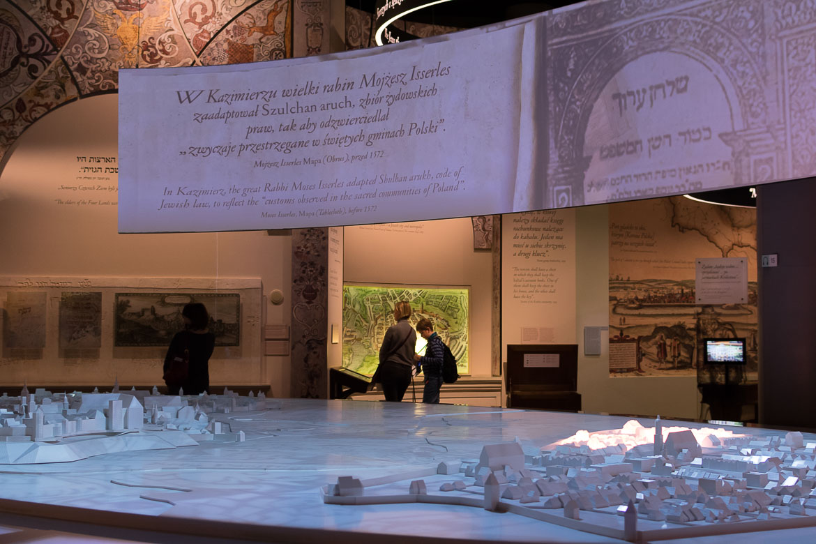 The photo shows the warm interior of POLIN Museum, the ideal place for a cold day during your winter in Warsaw city break. In the foreground, there's a scale model of Warsaw.