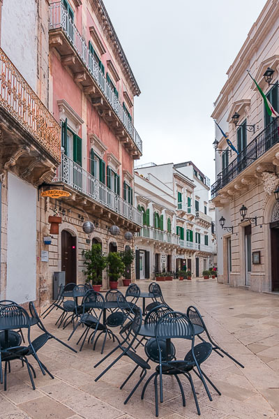 This image shows Martina Franca during siesta time. The town is completely empty. In the foreground, the tables and chairs of a cafe.