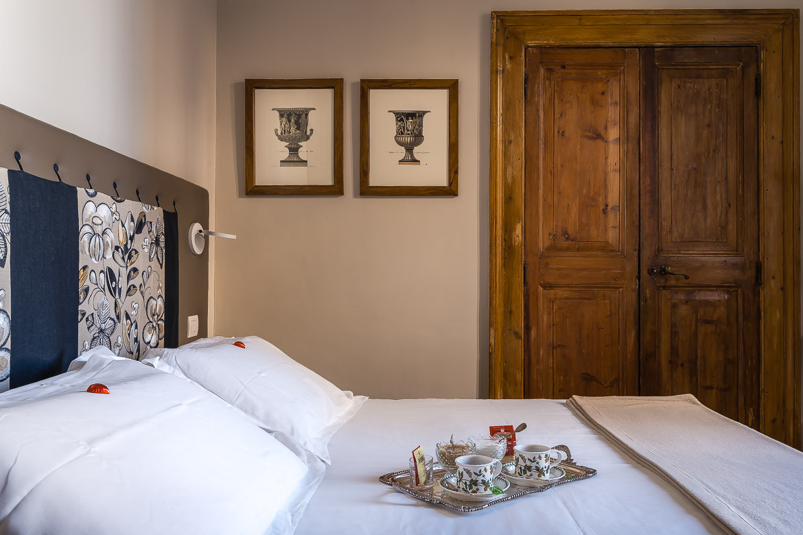 This image shows the interior of a hotel room in Rome. There's a double bed with white linen, chocolate hearts on the pillows and a silver tray with a tea set on the bed.