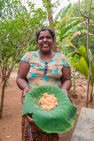 This image shows a Sri Lankan lady holding a dish she just prepared and smiling to the camera.