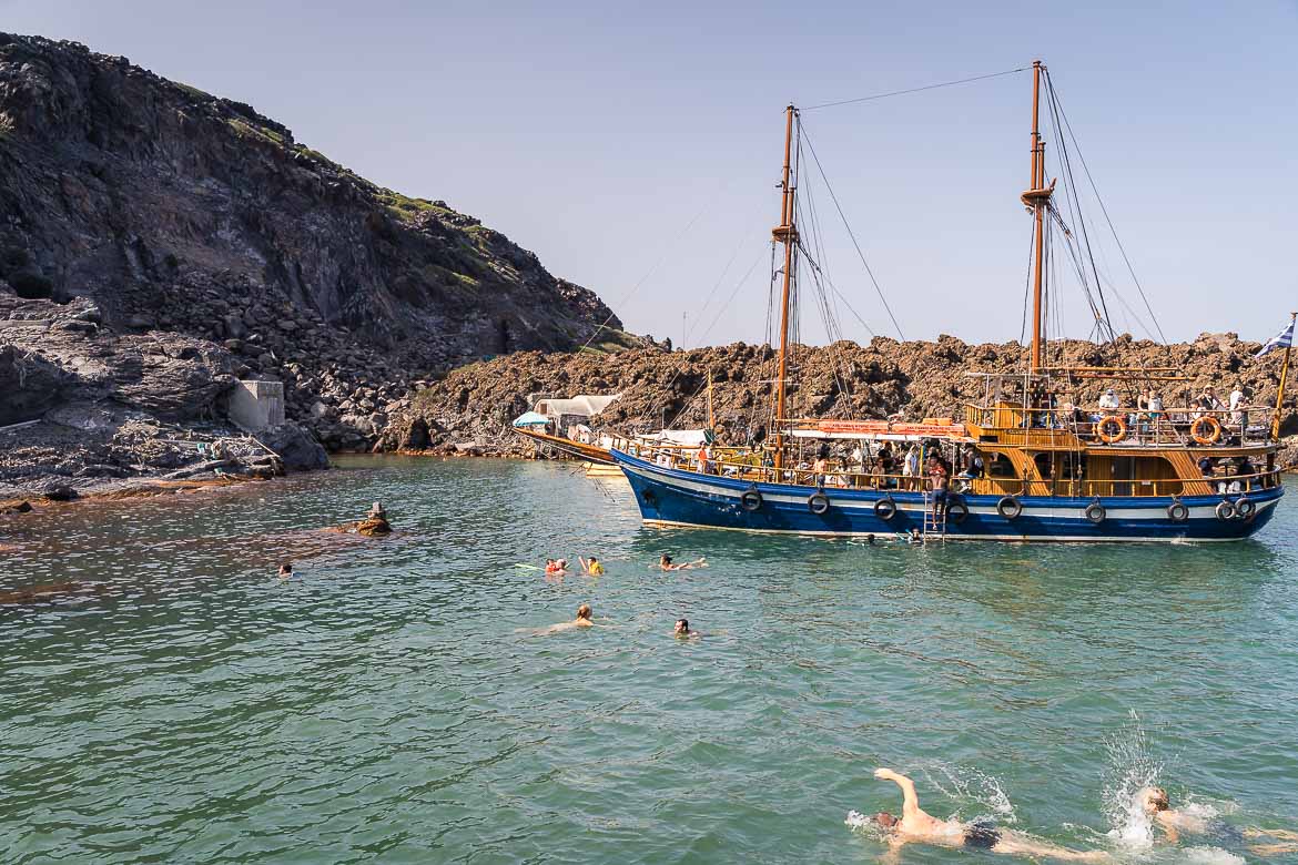 A wooden boat with two masts is moored near the hot springs. Tourists swim and enjoy the thermal waters.