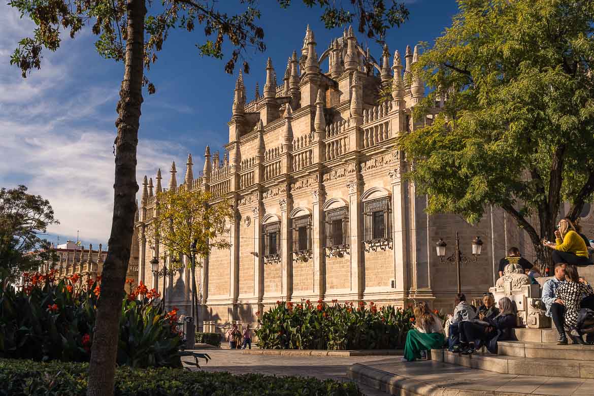 People rest on a square's steps next to Seville's Cathedral on a sunny day.