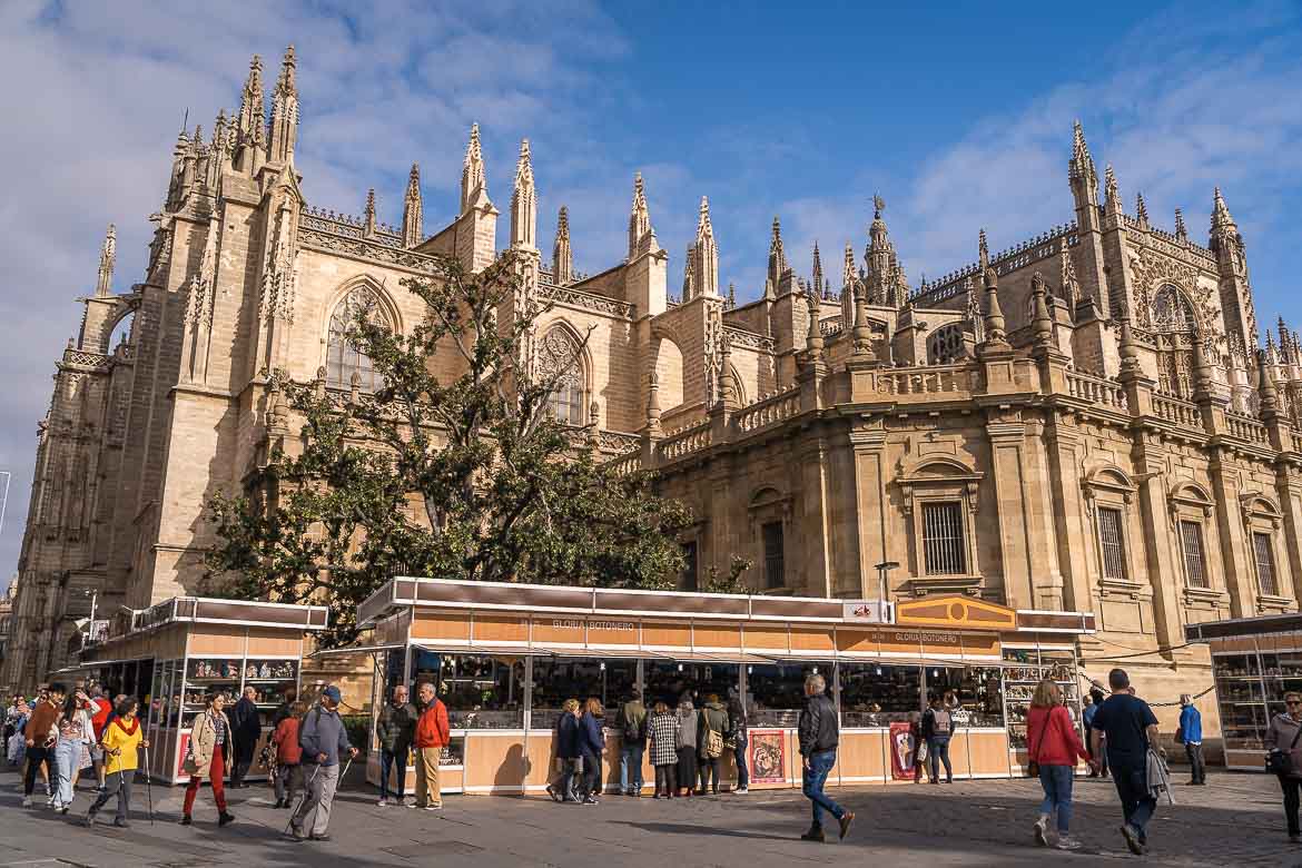 The Christmas market in front of Seville Cathedral on a sunny day. People in winter clothes are strolling around.