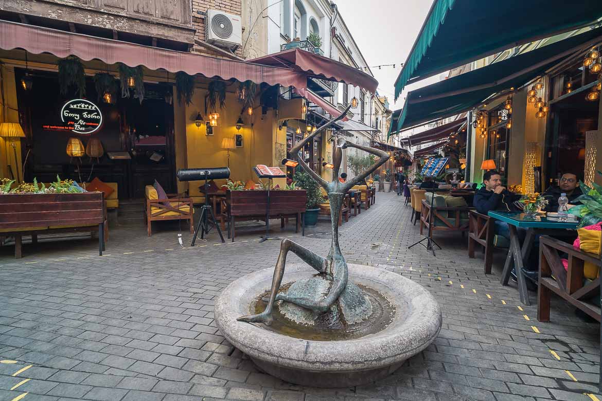 A small fountain with a sculpture on a street with cafés in the Old Town.