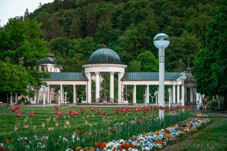 The colonnade with Karolina Spring. The colonnade is surrounded by forest. Tulips and flowers are in the background.