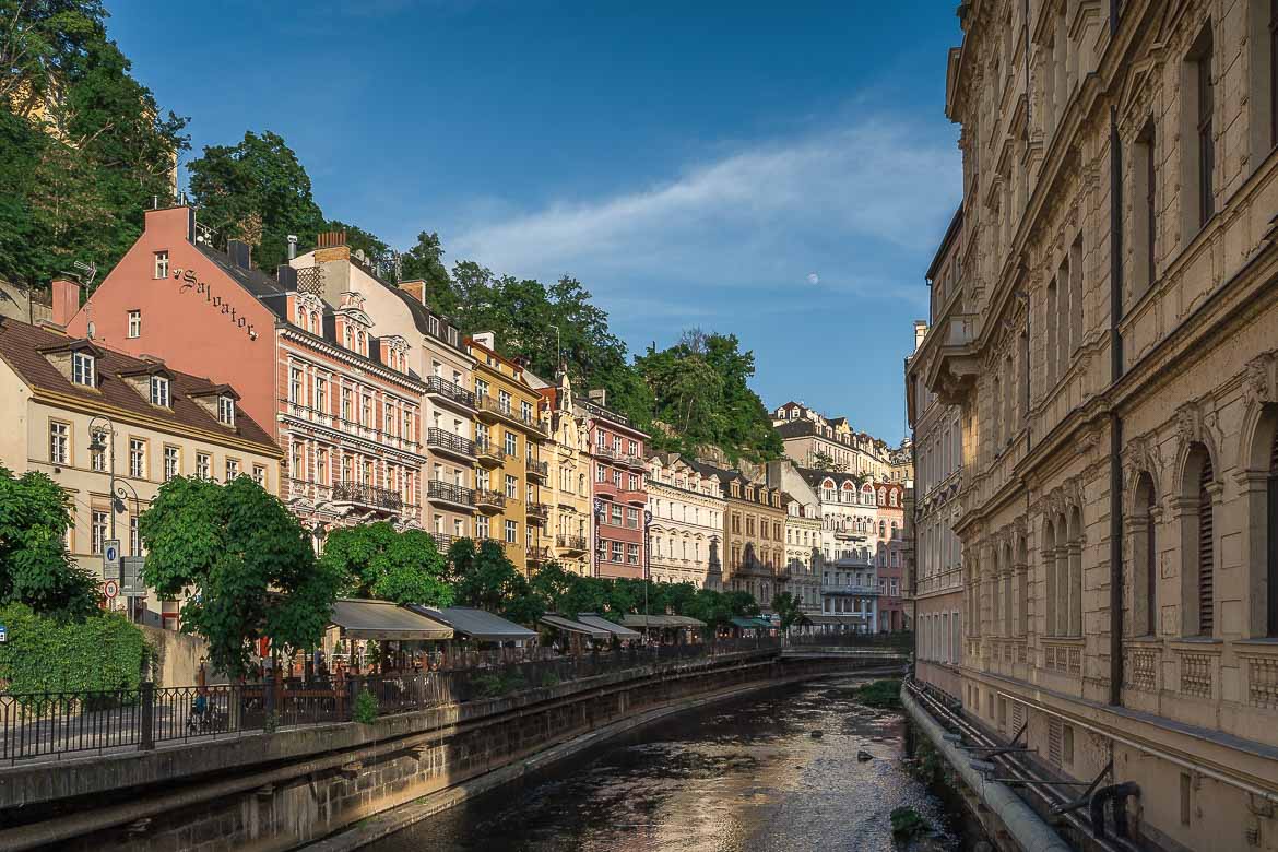 A panoramic view of the river from the bridge. On the right there are neoclassical buildings and on the left a promenade lined with restaurants and cafes.