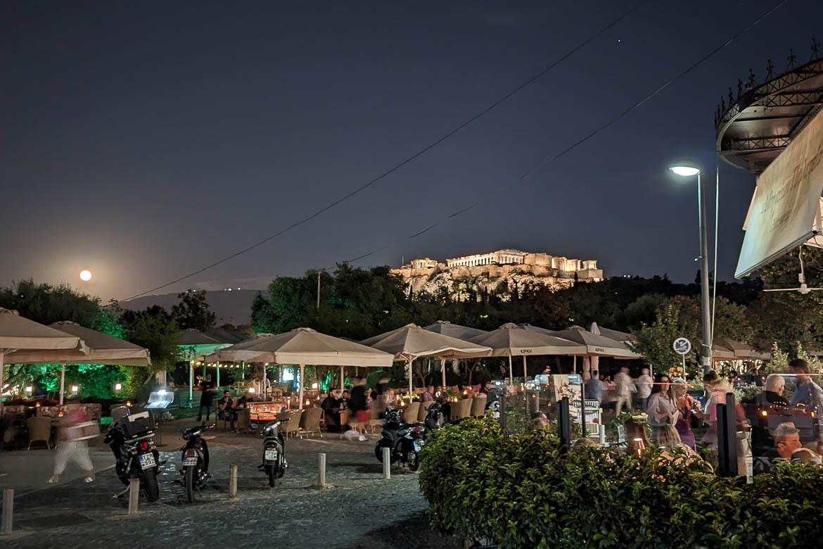 Apostolou Pavlou Street with its cafés and the illuminated Acropolis in the background on a full moon night.