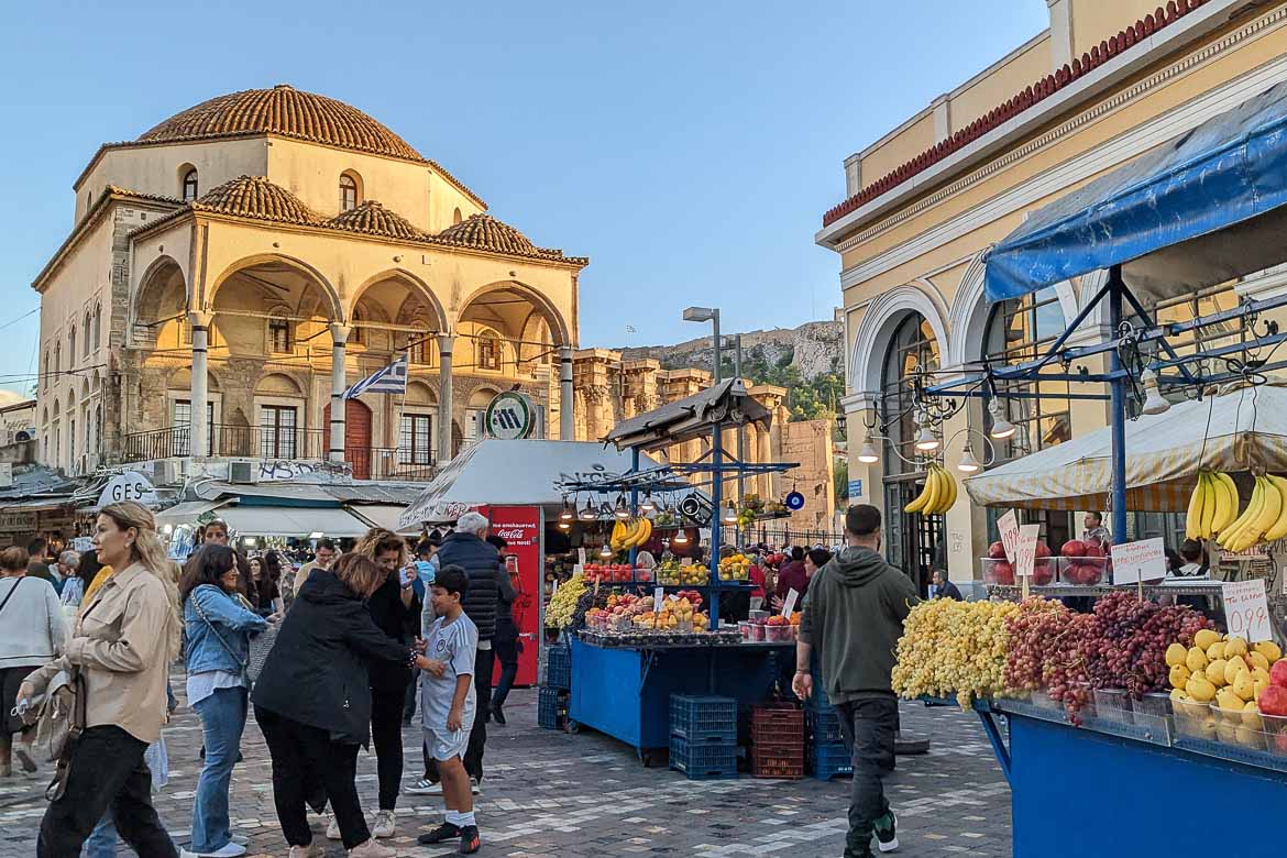 Monastiraki Square with stalls selling fruit. There are crowds outside the metro station.
