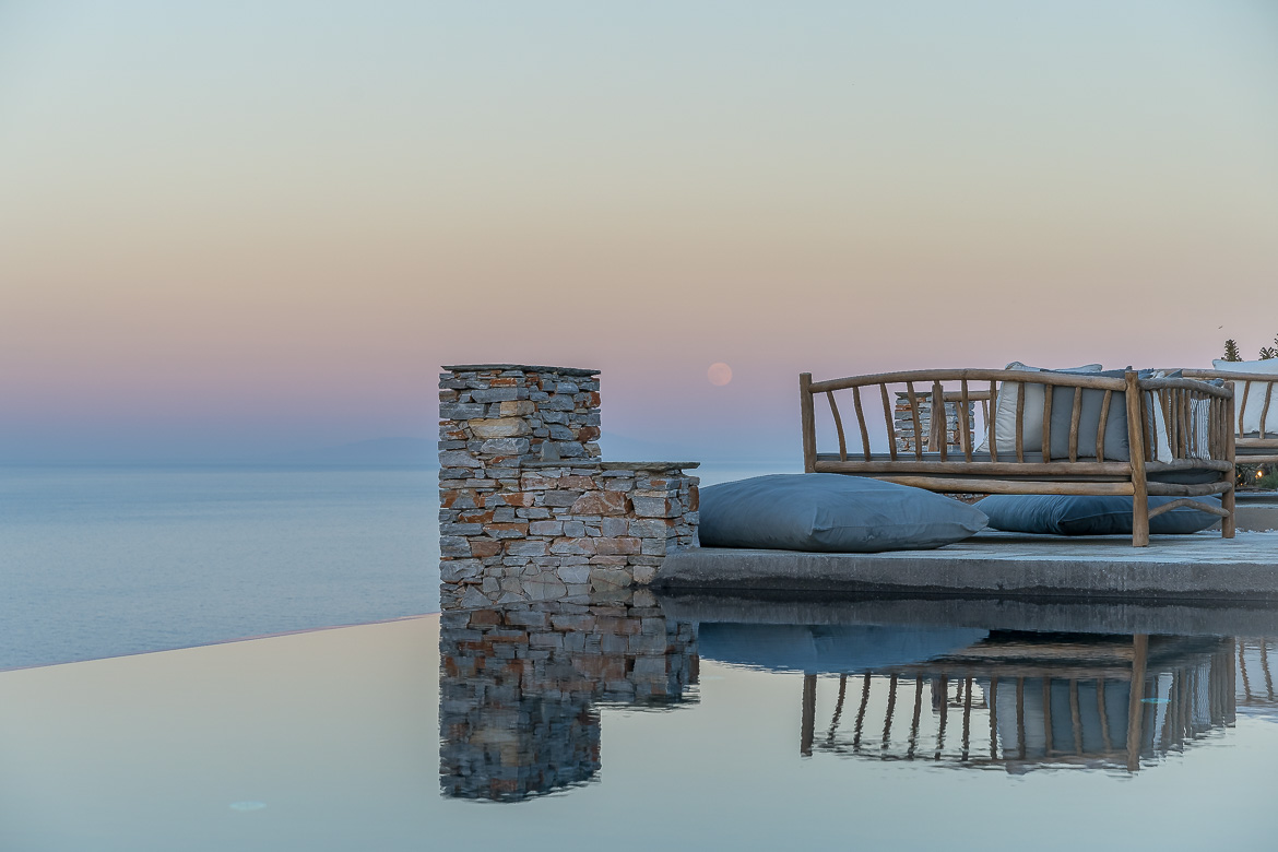 This image shows the infinity pool at Verina Astra Hotel at sunset with a rising full moon in the background.