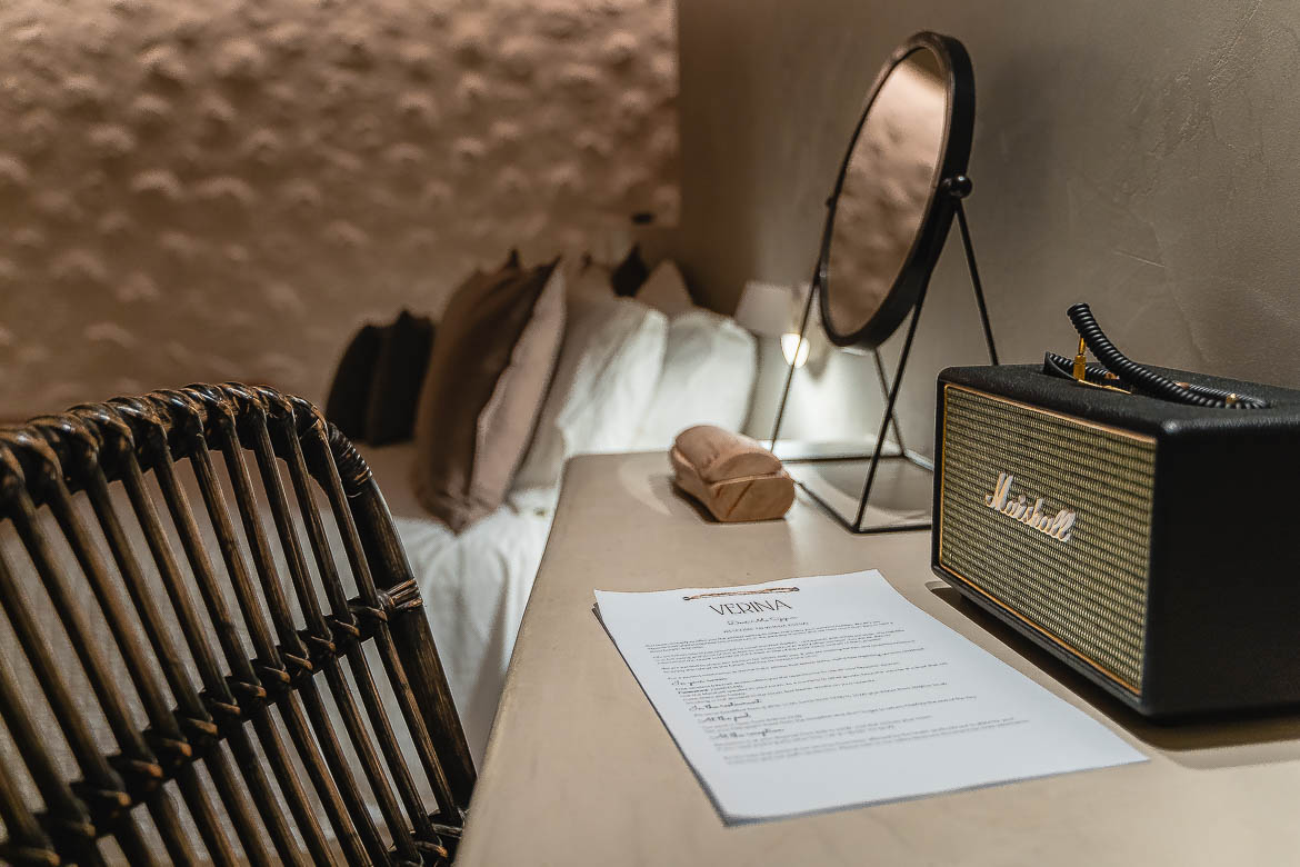 This is a close up of the desk area inside a suite. There's a Marshall radio and a sheet of paper with the Verina logo on it. In the background, the lush bed. 
