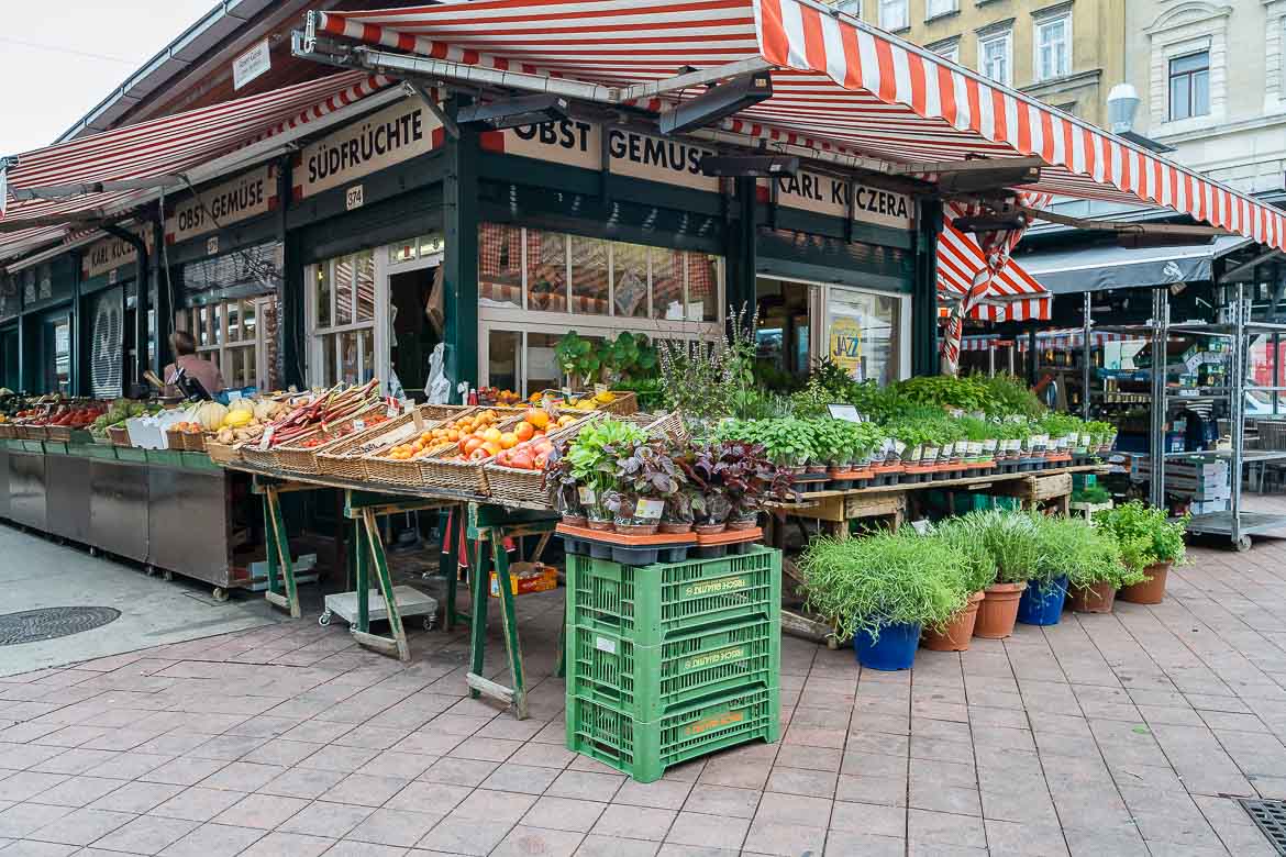 Stalls with fruit and vegetables in front of a green kiosk with a red and white tent in Naschmarkt.