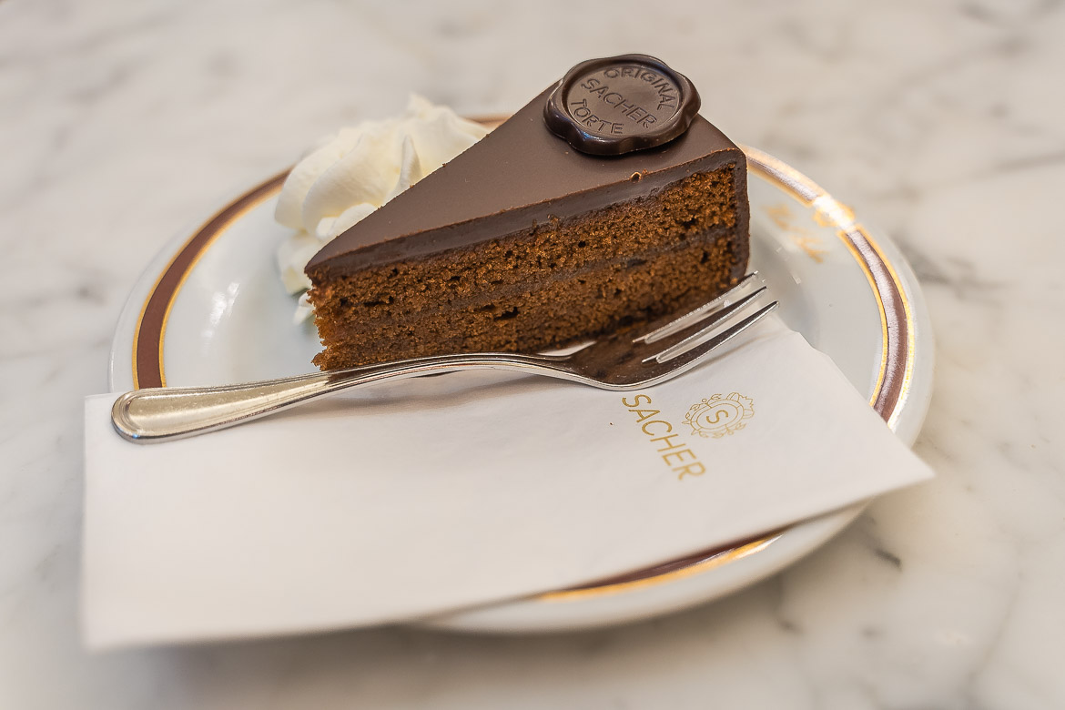 A Sachertorte with whipped cream on the side served on a small plate at Café Sacher.