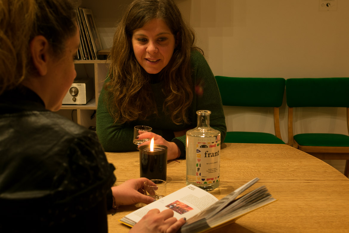 This image shows Maria and Katerina drinking vodka shots at their hotel while reading a Warsaw guidebook.