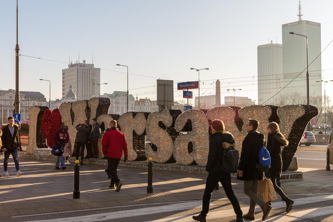 This is a huge I (heart) Warsaw sign with many people walking past it.
