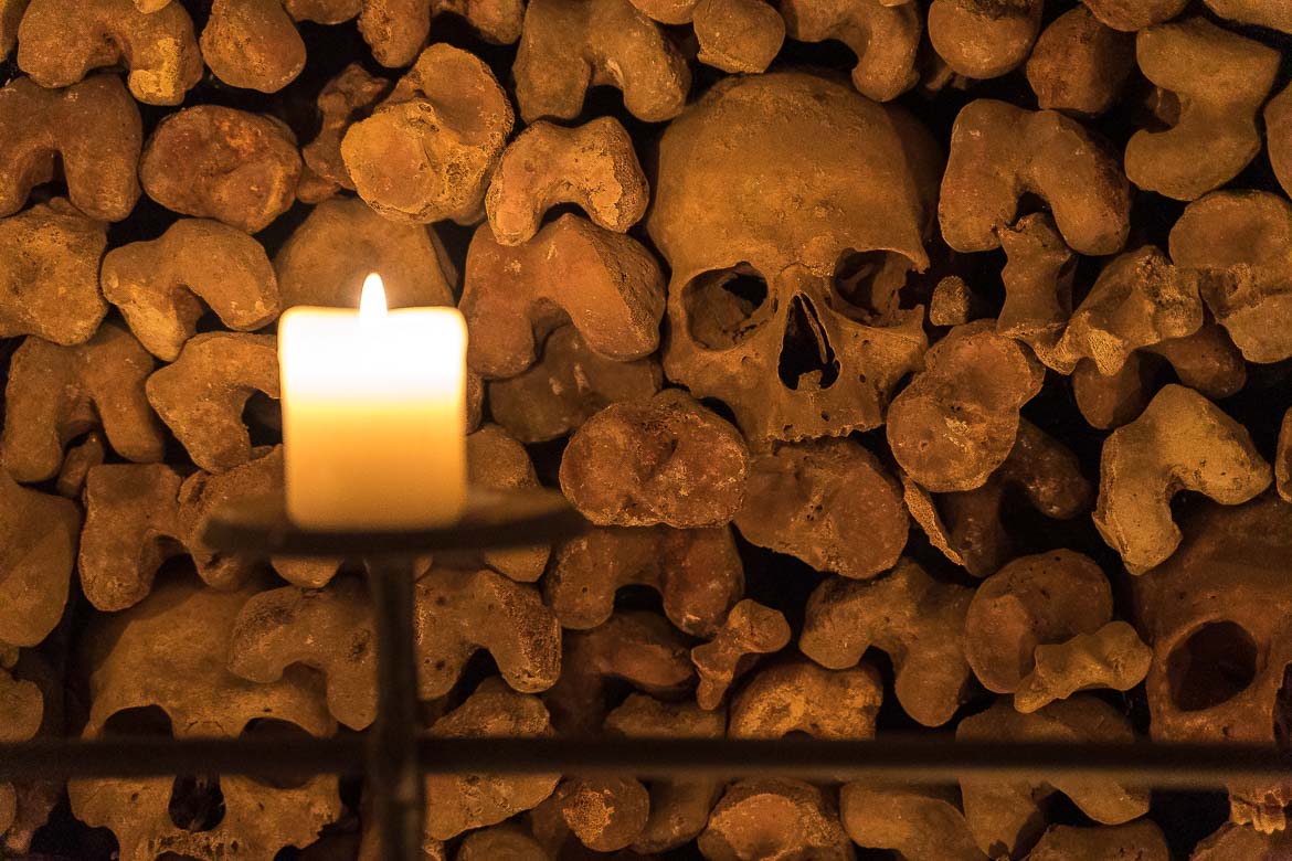 This image shows a skull and other bones in a room lit by a candle in the Brno Ossuary.