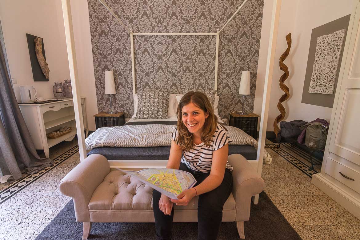 This is a photo of Katerina smiling at the camera with a map in her hand. She is sitting in front of a wonderful bed at one of the Junior Suites at Palazzo Bignami. 