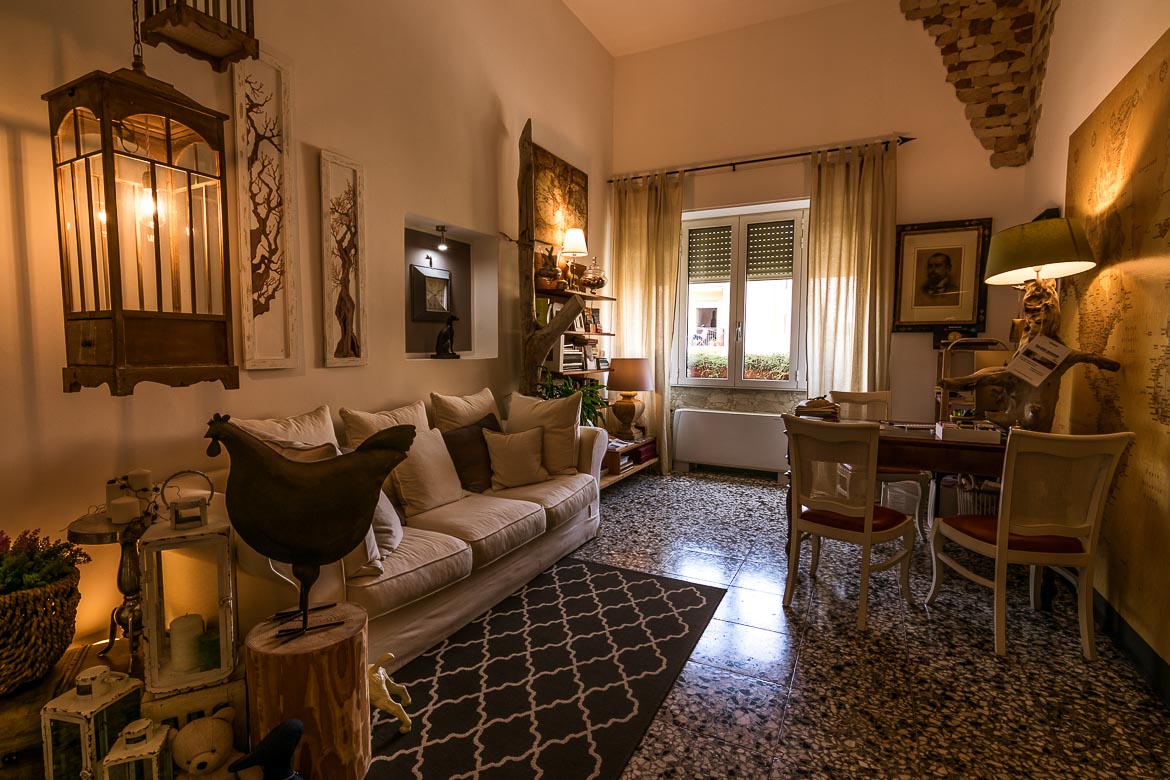 This photo shows the reception area at Palazzo Bignami. There is a cosy white sofa and a desk, warm lighting and french windows. The room is stylishly decorated. 