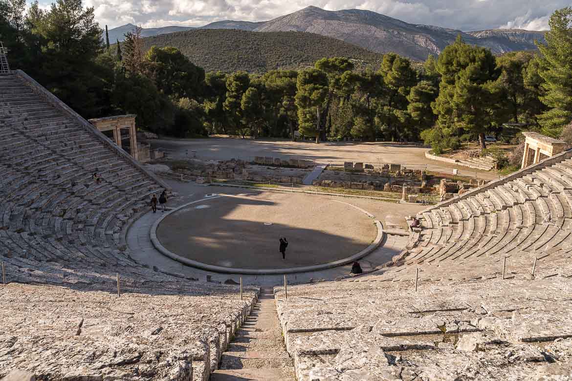 This image shows a panoramic view of the Ancient Theatre of Epidaurus. The photo is taken from the top rows of the theatre.