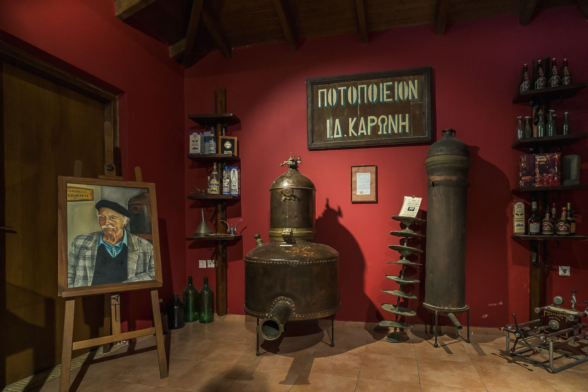 The museum of Karonis distillery. The painting of Karonis who founded the distillery is on the left of the room, old parts of the distillery are in the middle and bottles are on shelves across the wall.